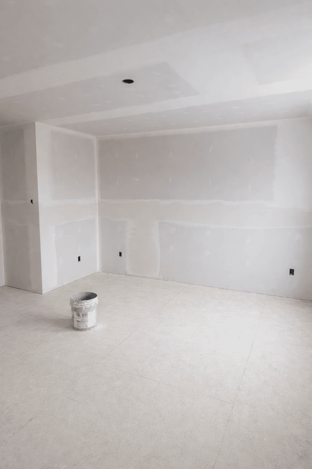 Empty room under construction with taped drywall seams and a bucket of joint compound.